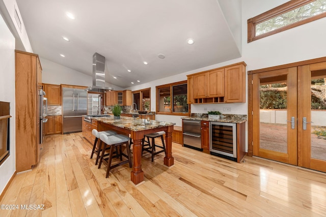 kitchen featuring a kitchen island with sink, island range hood, beverage cooler, a kitchen breakfast bar, and appliances with stainless steel finishes