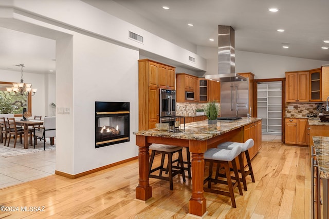 kitchen featuring visible vents, brown cabinetry, light stone counters, island exhaust hood, and stainless steel appliances