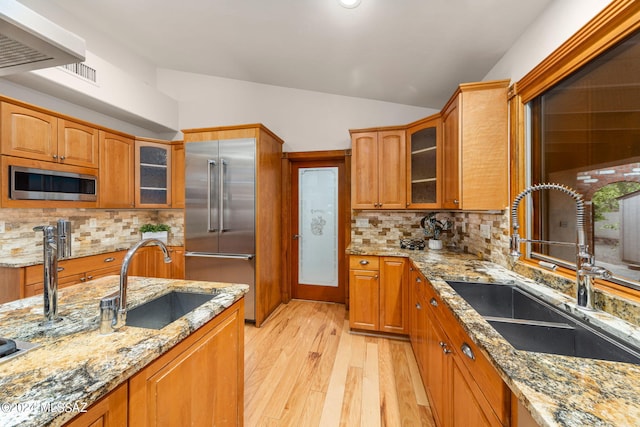 kitchen featuring brown cabinets, vaulted ceiling, stainless steel appliances, and a sink