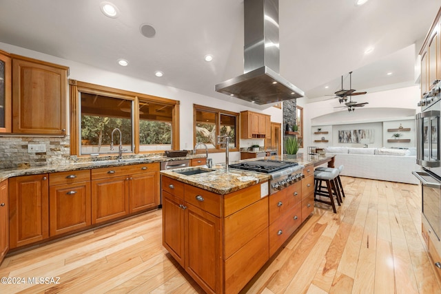 kitchen with a sink, island exhaust hood, a kitchen island with sink, and stainless steel gas cooktop