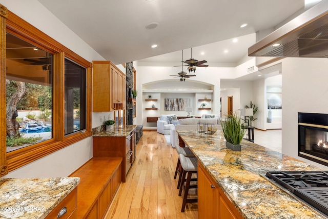 kitchen with extractor fan, stainless steel gas cooktop, light wood-style floors, open floor plan, and a glass covered fireplace