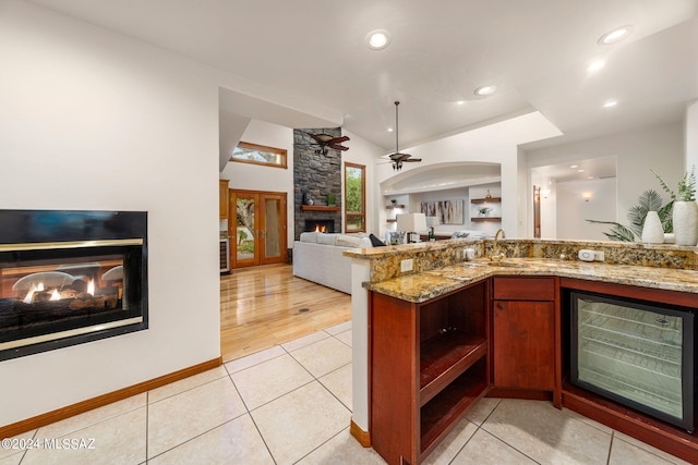 kitchen featuring light tile patterned floors, light stone counters, a fireplace, vaulted ceiling, and open floor plan