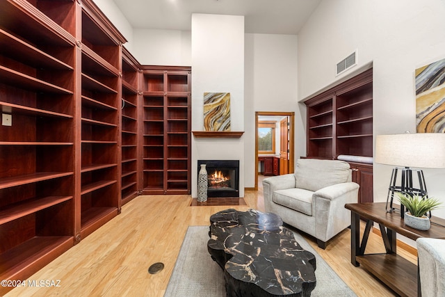 sitting room featuring a fireplace with flush hearth, a towering ceiling, wood finished floors, and visible vents