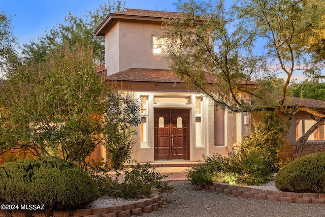 entrance to property featuring roof with shingles and stucco siding