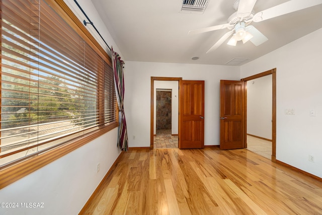 unfurnished bedroom featuring a ceiling fan, visible vents, light wood-style flooring, and baseboards