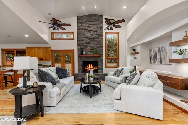 living room featuring light wood-style floors, ceiling fan, a stone fireplace, and high vaulted ceiling