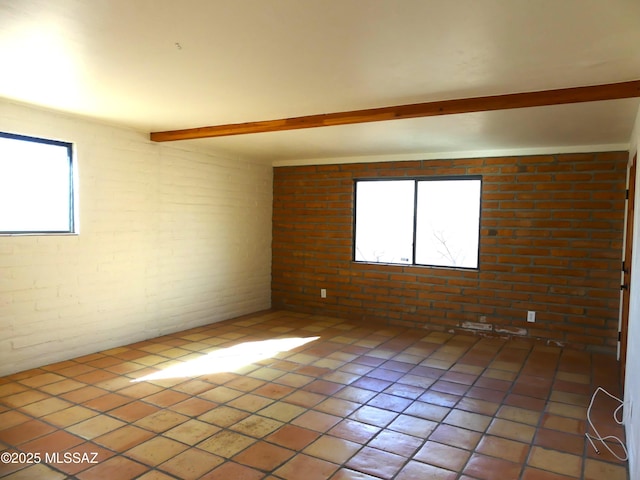 unfurnished room with beamed ceiling and brick wall