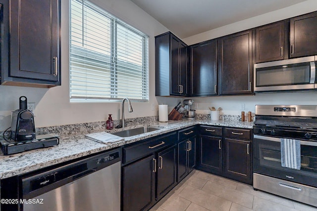 kitchen featuring appliances with stainless steel finishes, sink, light tile patterned floors, dark brown cabinetry, and light stone countertops