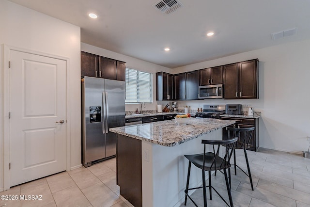 kitchen featuring appliances with stainless steel finishes, a kitchen bar, a center island, and dark brown cabinets