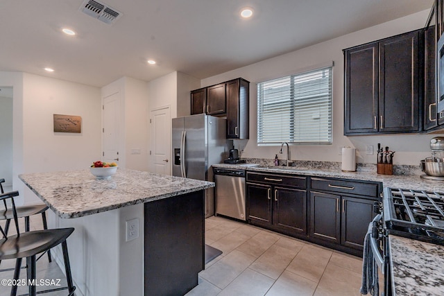 kitchen with a kitchen island, sink, a breakfast bar area, light stone counters, and stainless steel appliances