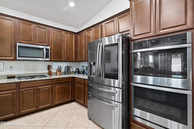 kitchen with lofted ceiling, light stone countertops, stainless steel appliances, and light tile patterned flooring