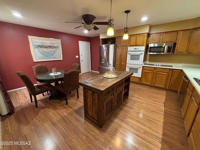 kitchen with appliances with stainless steel finishes, pendant lighting, a center island, ceiling fan, and light wood-type flooring