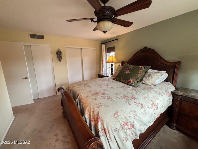 bedroom with two closets, light colored carpet, and ceiling fan