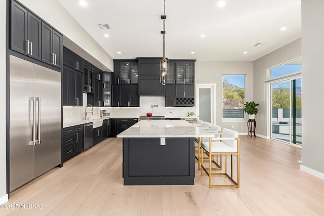 kitchen with pendant lighting, appliances with stainless steel finishes, light stone countertops, light hardwood / wood-style floors, and a kitchen island