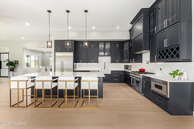 kitchen with a large island with sink, a breakfast bar area, built in appliances, and decorative light fixtures