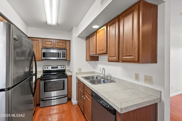 kitchen with appliances with stainless steel finishes, tile counters, sink, and light hardwood / wood-style flooring