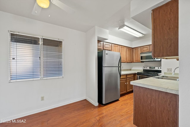 kitchen featuring sink, light hardwood / wood-style flooring, ceiling fan, stainless steel appliances, and tile counters