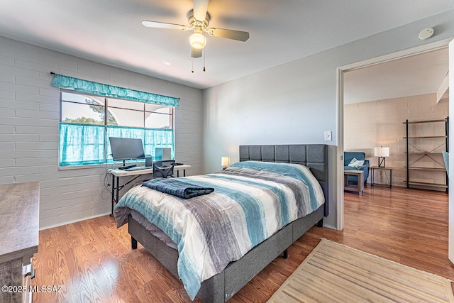 bedroom with ceiling fan, hardwood / wood-style flooring, and brick wall