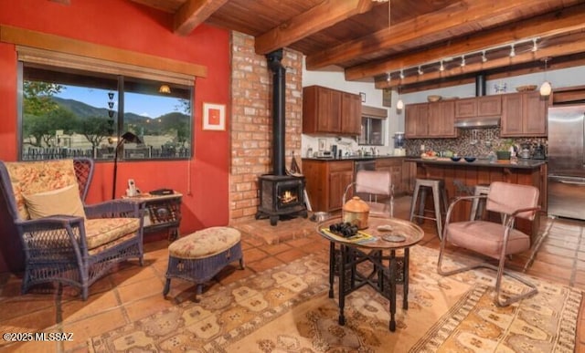 living room featuring beamed ceiling, a wood stove, light tile patterned floors, a mountain view, and wooden ceiling