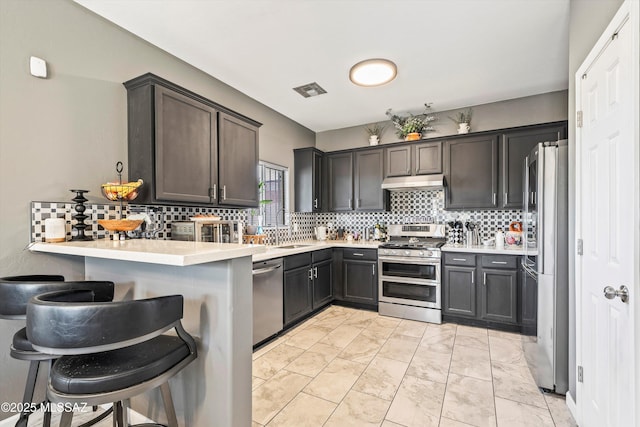 kitchen featuring dark brown cabinetry, a kitchen bar, kitchen peninsula, and appliances with stainless steel finishes