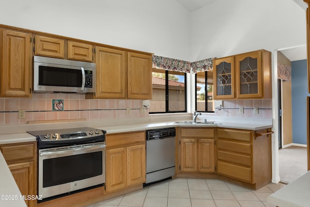 kitchen featuring sink, light tile patterned floors, appliances with stainless steel finishes, a towering ceiling, and decorative backsplash