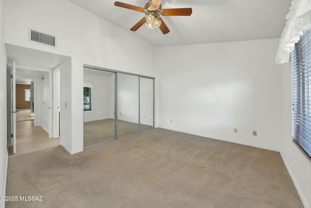 unfurnished bedroom with light carpet, a closet, ceiling fan, and a high ceiling