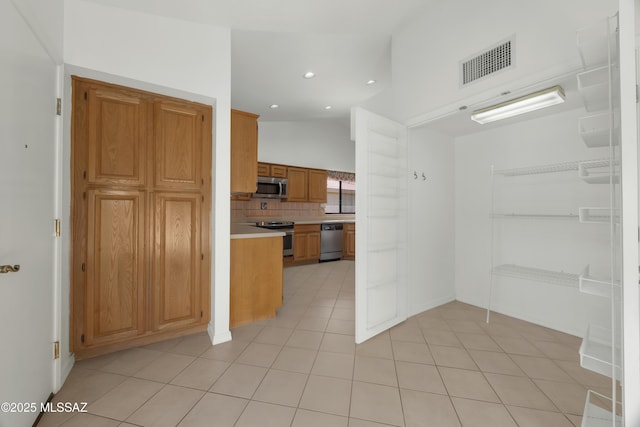 kitchen featuring tasteful backsplash, light tile patterned floors, stainless steel appliances, and lofted ceiling