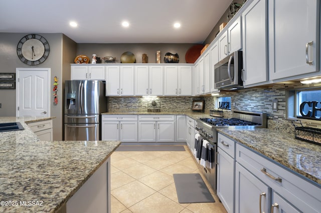 kitchen with light tile patterned flooring, light stone countertops, white cabinets, and appliances with stainless steel finishes