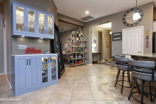 bar featuring blue cabinets, decorative light fixtures, light stone countertops, and light tile patterned flooring