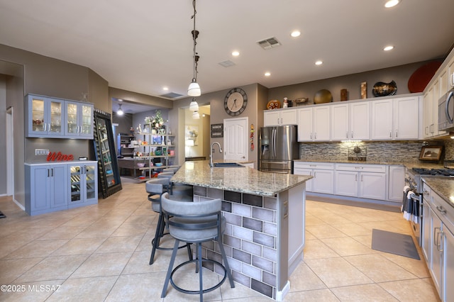 kitchen with sink, appliances with stainless steel finishes, pendant lighting, a kitchen island with sink, and white cabinets