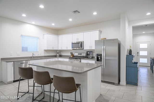 kitchen with a kitchen island, a breakfast bar, sink, white cabinets, and stainless steel appliances