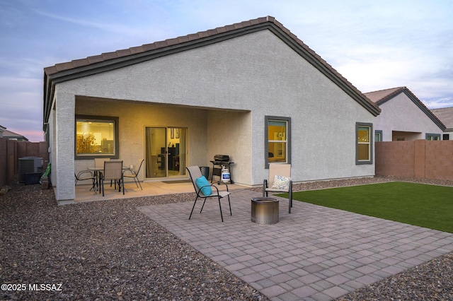 back house at dusk with a lawn, cooling unit, and a patio area