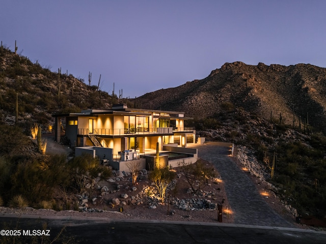 back house at dusk with a patio, a mountain view, and a balcony