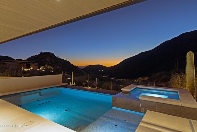 pool at dusk with a mountain view and an in ground hot tub