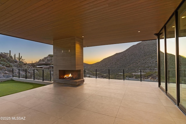 patio terrace at dusk featuring a fireplace and a mountain view