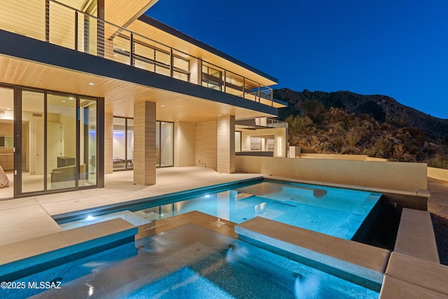 pool at twilight with an in ground hot tub, a mountain view, and a patio