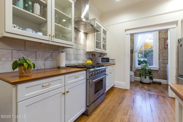 kitchen featuring butcher block countertops, range hood, tasteful backsplash, white cabinets, and high end stainless steel range oven