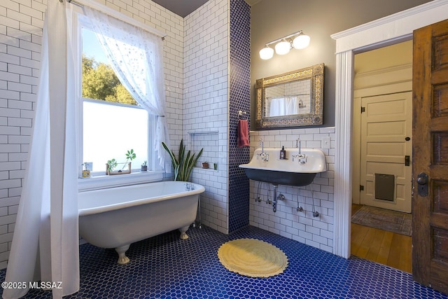 bathroom featuring tile patterned floors, a tub to relax in, sink, and tile walls