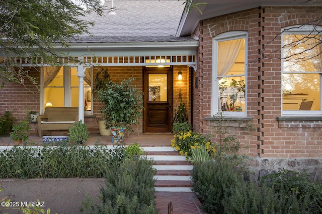 property entrance featuring brick siding, a porch, and a shingled roof