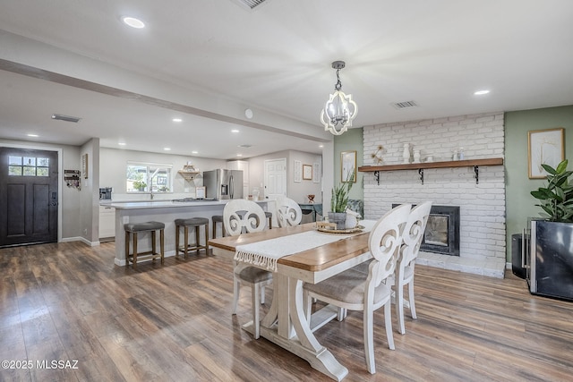 dining area with hardwood / wood-style flooring, a chandelier, and a brick fireplace