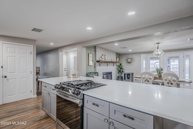 kitchen with pendant lighting, dark wood-type flooring, stainless steel gas range, gray cabinets, and a brick fireplace