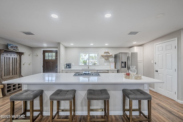 kitchen with appliances with stainless steel finishes, sink, white cabinets, a kitchen bar, and hardwood / wood-style flooring