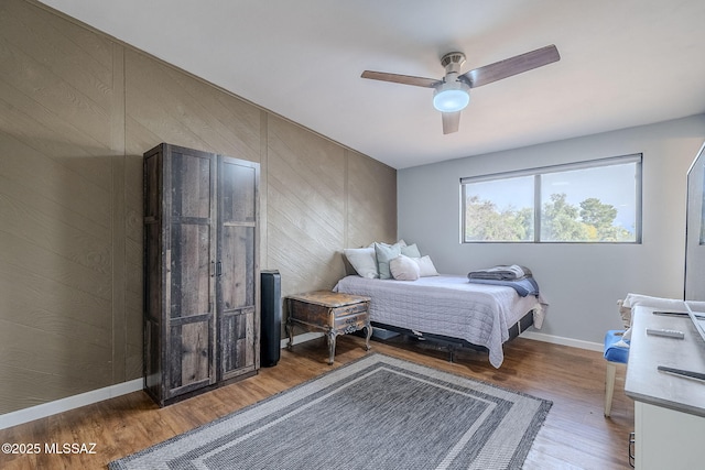 bedroom with ceiling fan, hardwood / wood-style floors, and wood walls