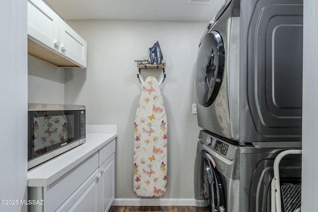 washroom with dark wood-type flooring, cabinets, and stacked washer / dryer