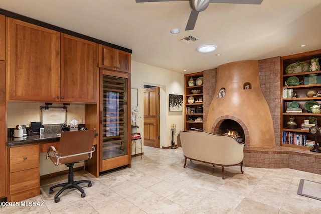 tiled office space with a brick fireplace, built in desk, built in features, and ceiling fan