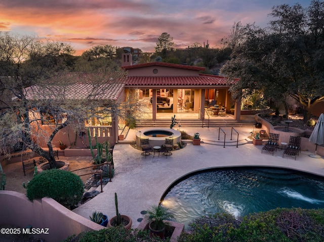 pool at dusk with a hot tub and a patio area