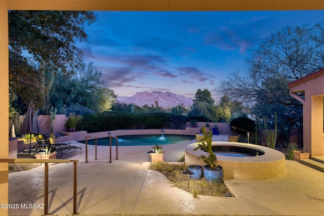 pool at dusk with a patio, a mountain view, pool water feature, and an in ground hot tub