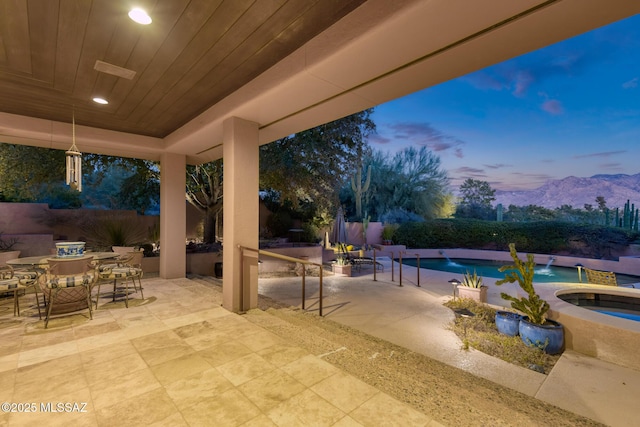 patio terrace at dusk featuring a swimming pool with hot tub, a mountain view, and pool water feature