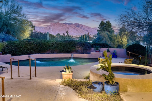 pool at dusk with an in ground hot tub, pool water feature, a mountain view, and a patio