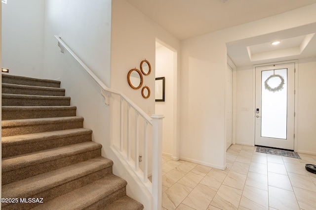 entryway with stairs, baseboards, and a raised ceiling